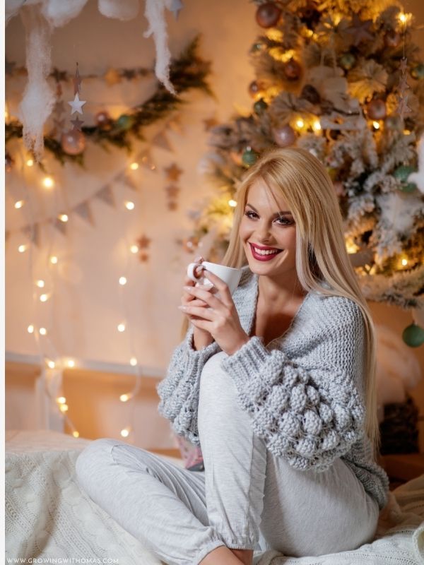 Woman-wearing-a-cozy-Christmas-sweater-holding-a-mug-beside-a-Christmas-tree-in-christmas-photo-shoot-ideas